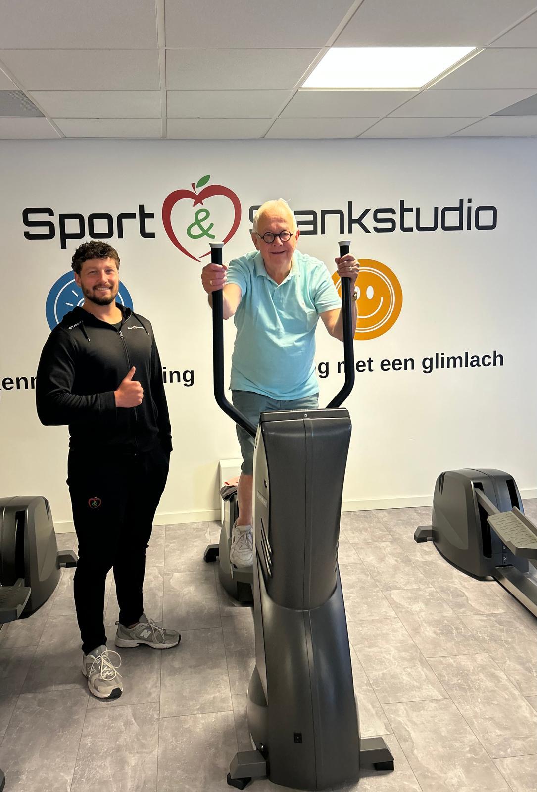 Man traint op een crosstrainer naast een coach bij Sport & Slankstudio.